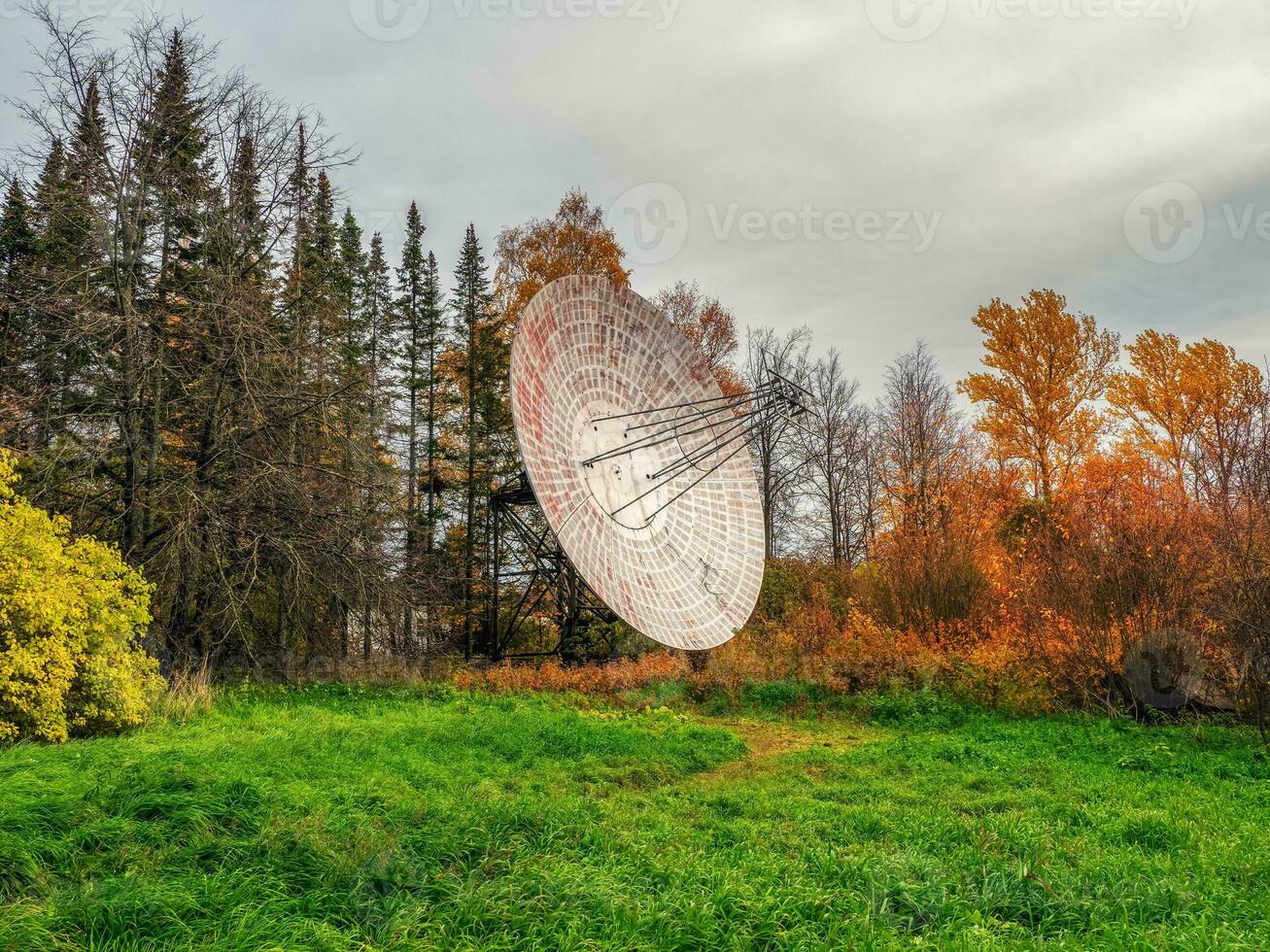 Vintage Radio Telescope, a large satellite dish on a background of observation forest and cloudy sky, radar in the past. Technology concept, search for extraterrestrial life, wiretap of space. photo