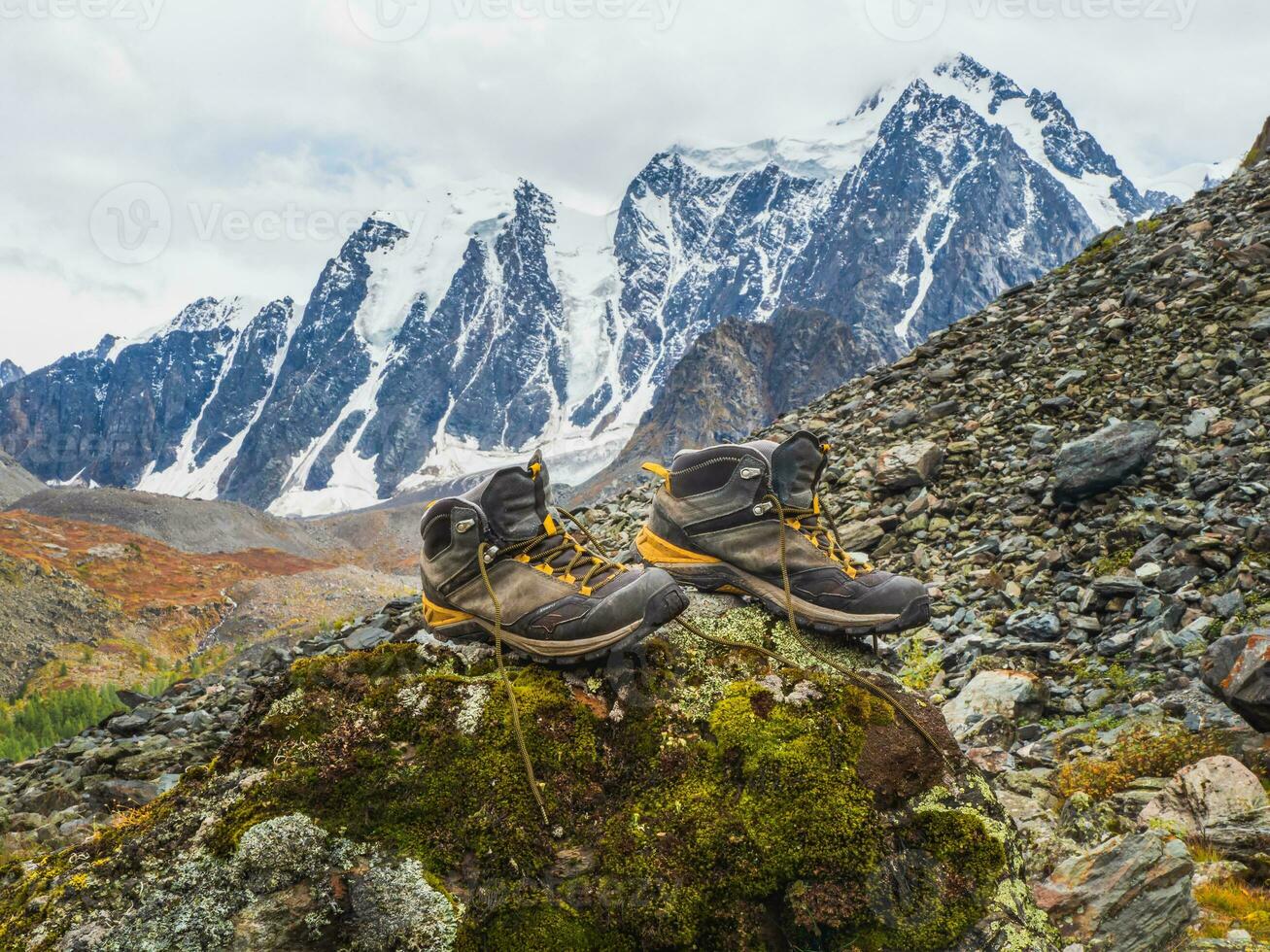 Wet hiking boots dry on a stone against the background of snow-covered high mountains. The difficulties of hiking, drying clothes in nature. photo