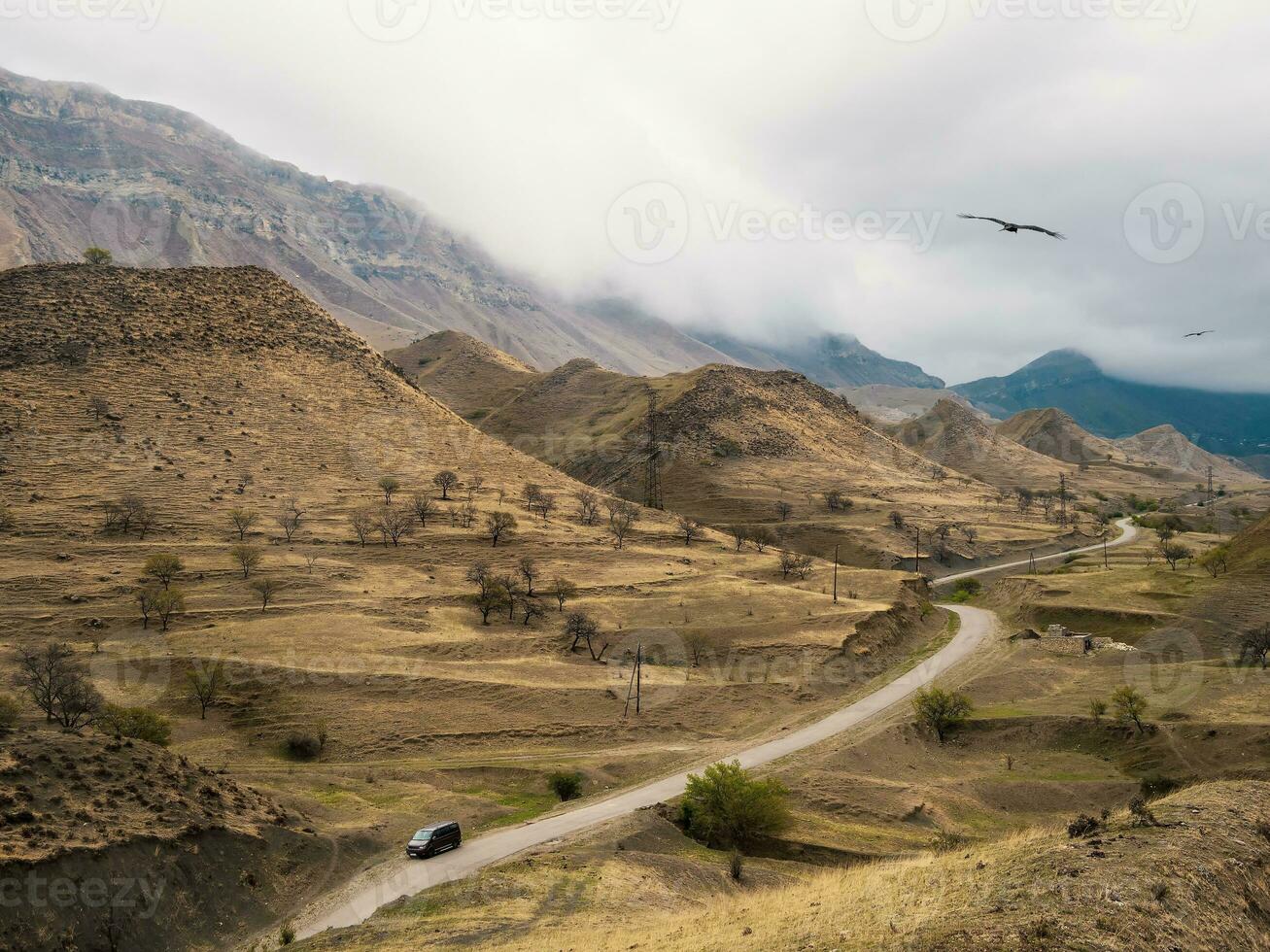 Rainy mountain plateau. Mountain terrain with a small minibus near the mountain. High mountains, complex mountain landscape, green terraces covered with sparse vegetation slopes. Dagestan. Russia. photo