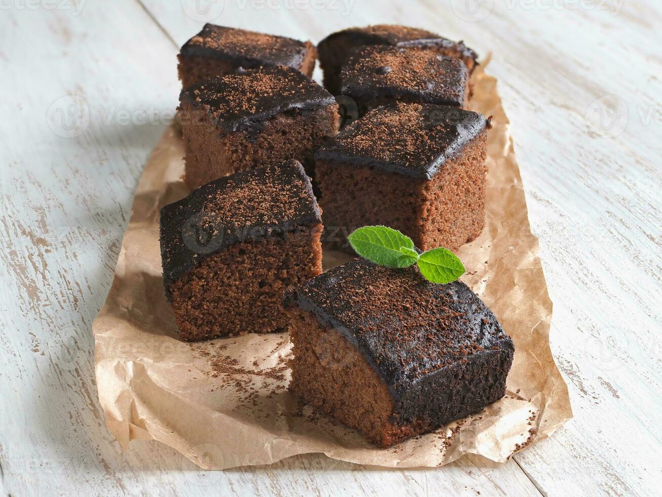 Freshly baked classic brownie on parchment are laid out on a white wooden surface. photo