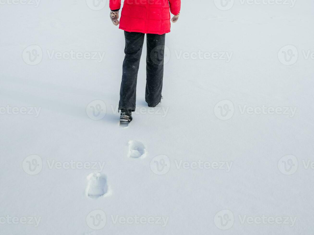 Woman in the red jacket walking on snow, footprints in snow, behind photo