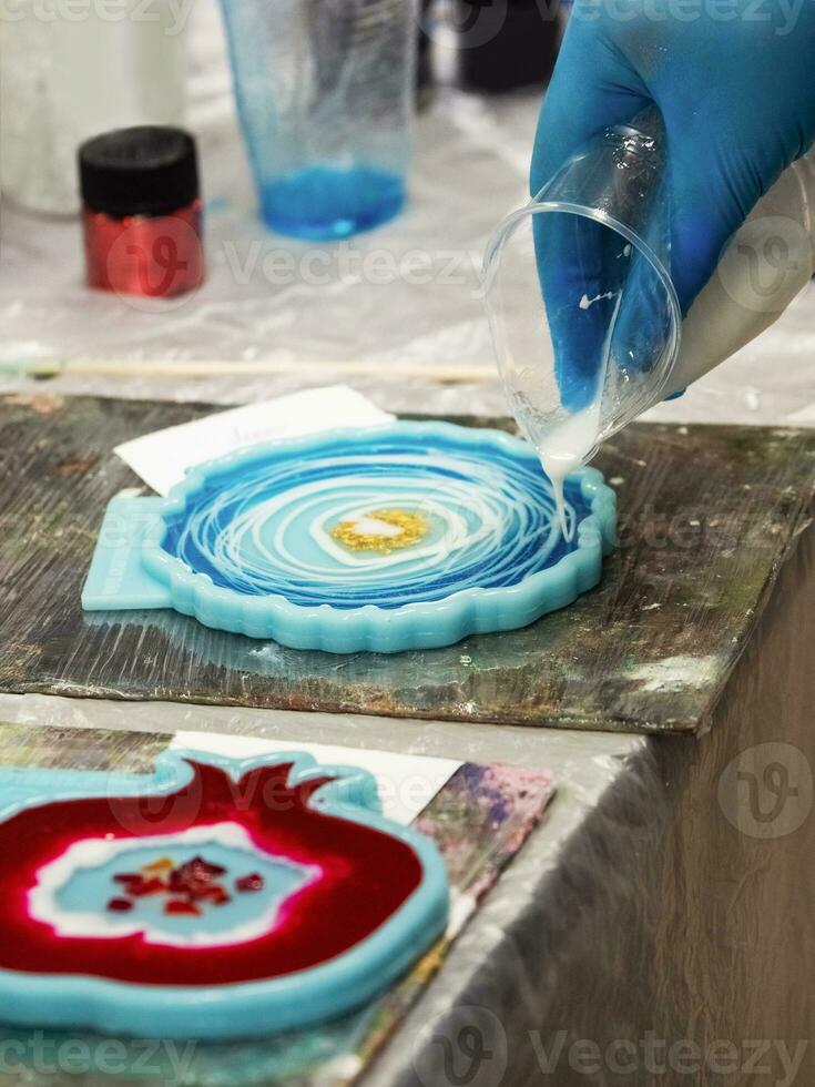 The art process of pouring epoxy resin into a wooden toy. Technology process of creating a painting in style resin art, works with epoxy in studio, makes a wooden stand with the image. Close up. photo