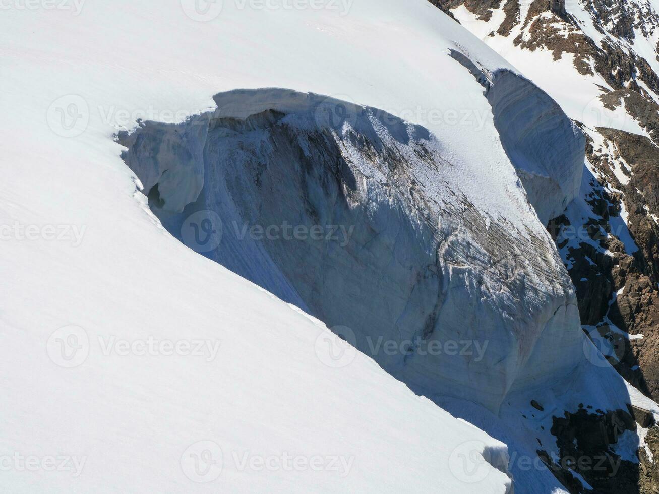 Dangerous snow ledge on the top of the mountain. Ledges from the snowy mountains. Cliffs and large rocks. Dangerous terrain. photo