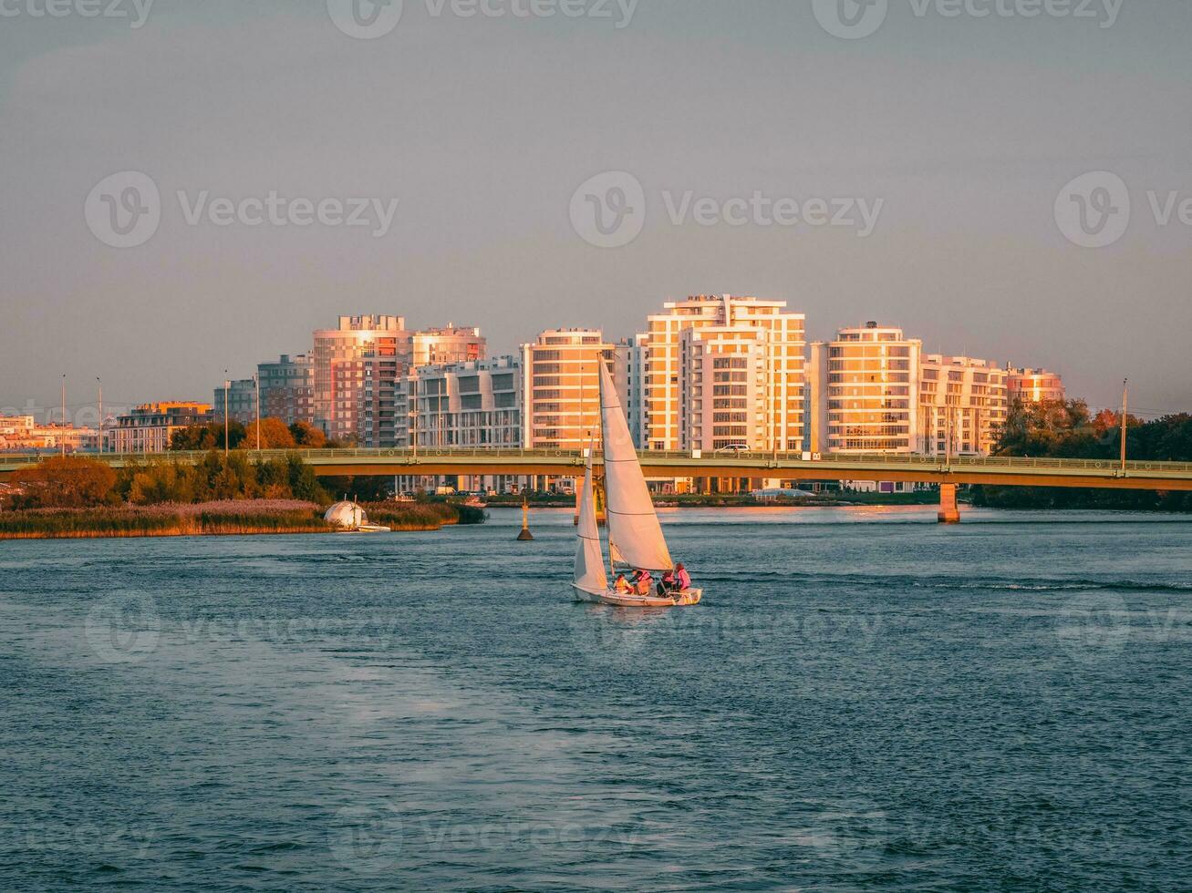 A yacht with sails drifts on the river against the background of a residential neighborhood with high-rise buildings. Saint-Petersburg. photo