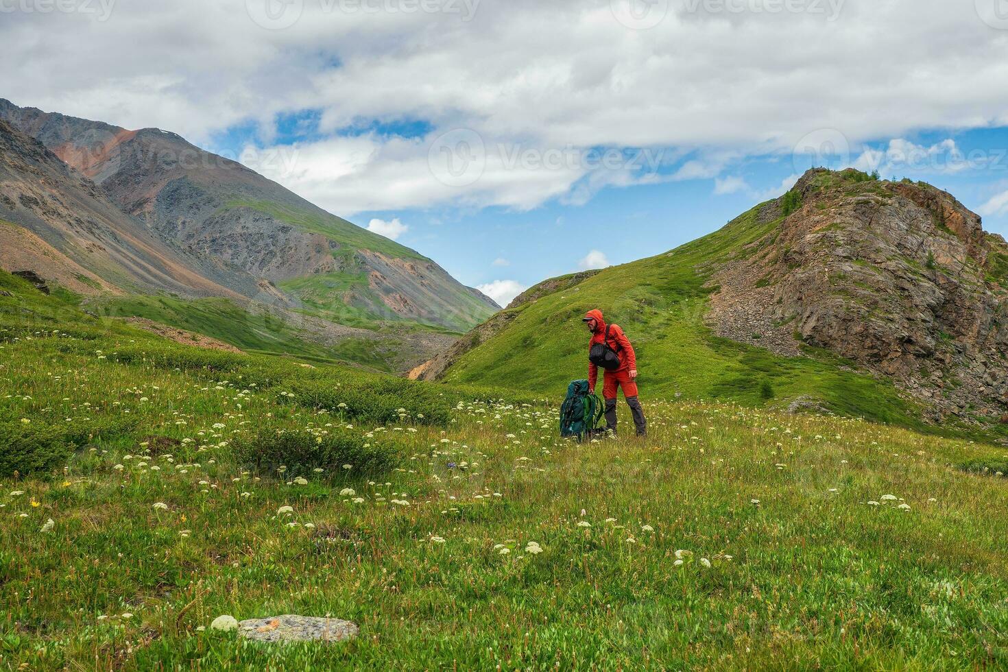Tired hiker man puts on a big heavy backpack. Rest time on a hike, a rest stop. Travel lifestyle, hiking hard track. photo