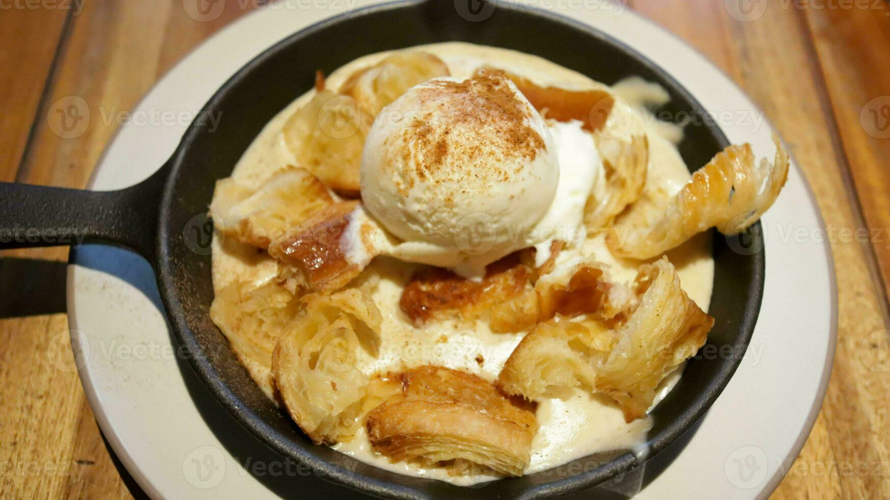 Croissant bread pudding with custard creamy sauce and vanilla ice cream topped with a little bit espresso coffee very delicious dessert present in a large pan. photo