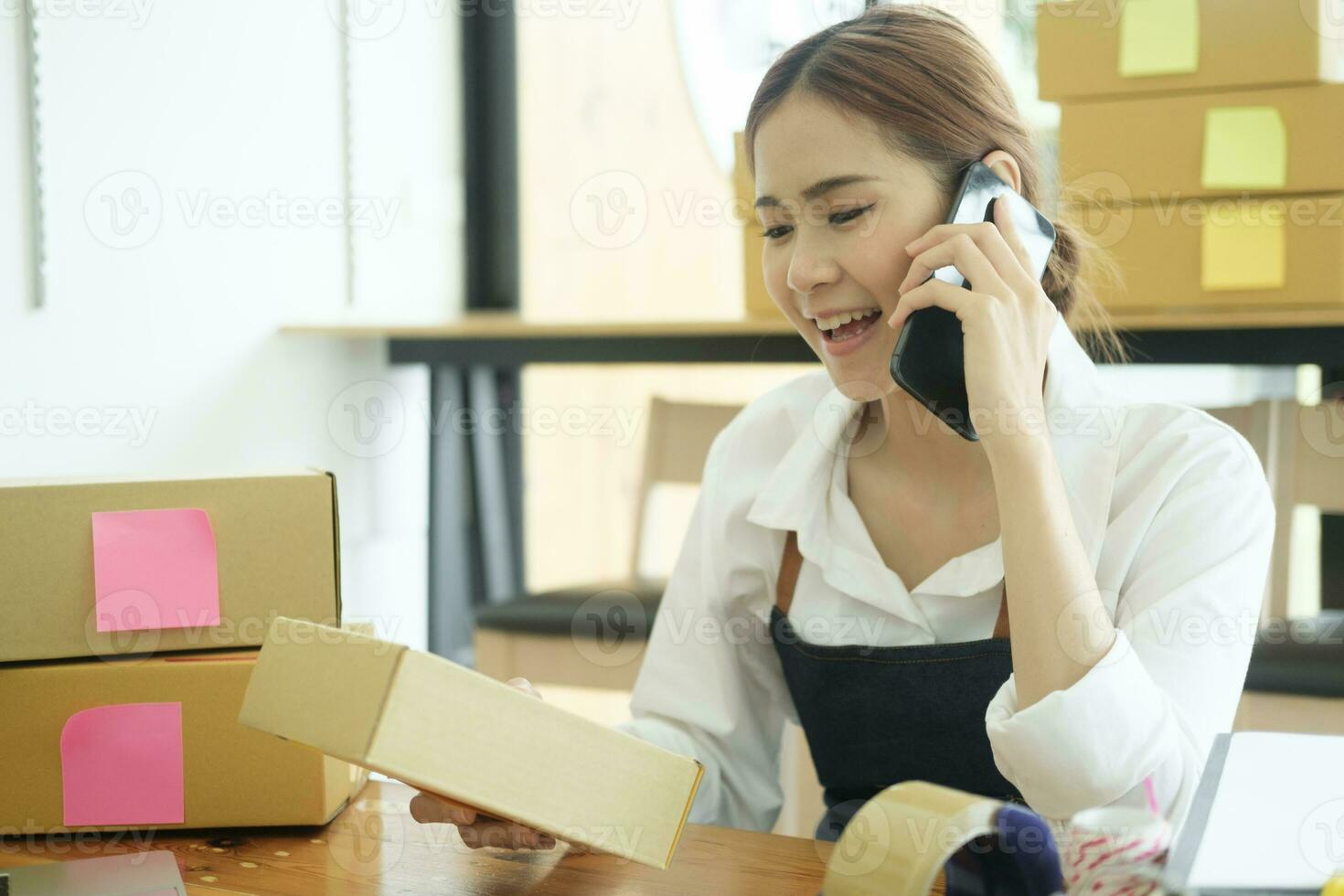 Asian female clothes shop owner folding a t-shirt and packing in a cardboard parcel box. photo