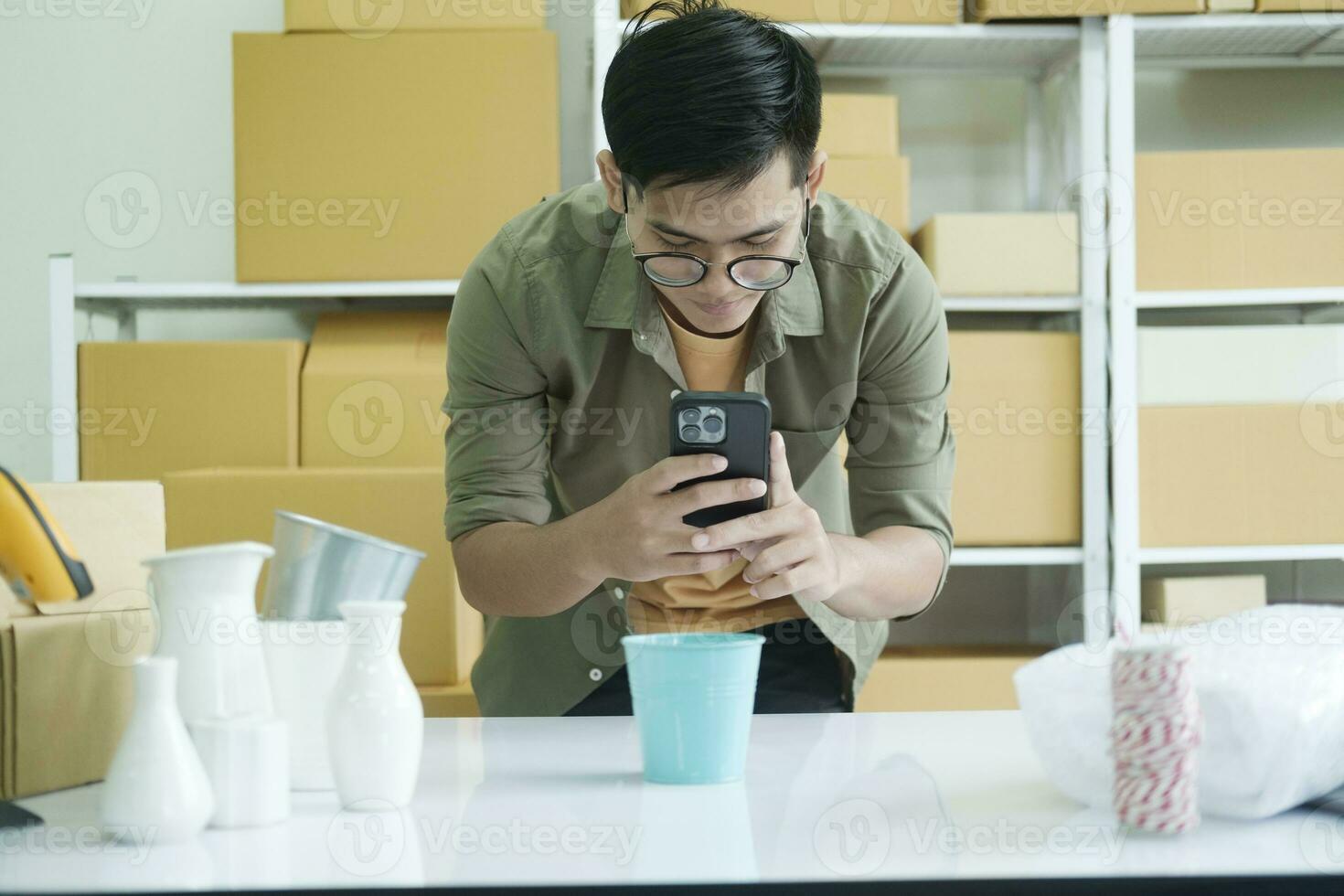 joven masculino en línea negocio propietario utilizando Teléfono móvil comprobación paquete o empaquetar caja. foto