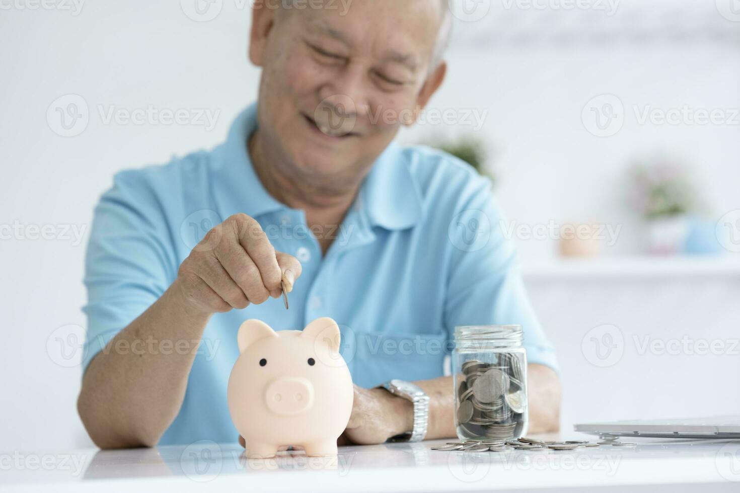 Elder man smiling putting a coin inside piggy bank. photo