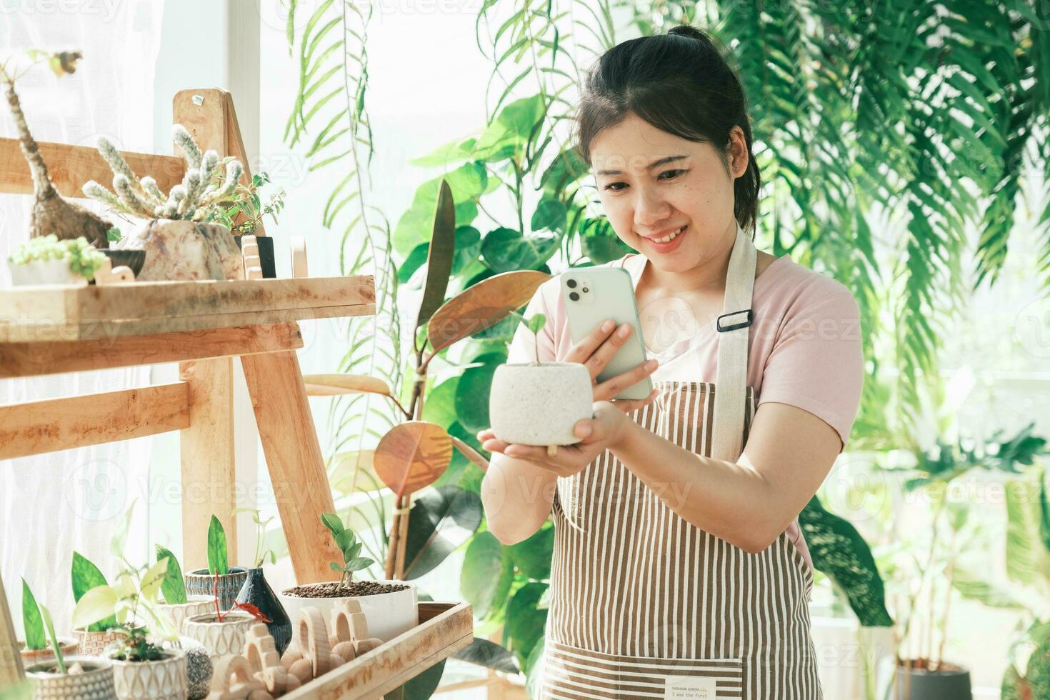 Smiling young woman taking smartphone picture of plant in a small shop photo