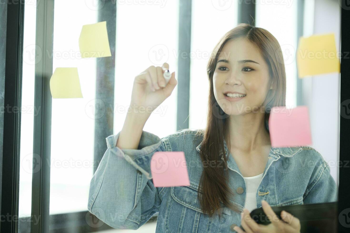 Young female student writing study plans on post-its on glass wall. photo