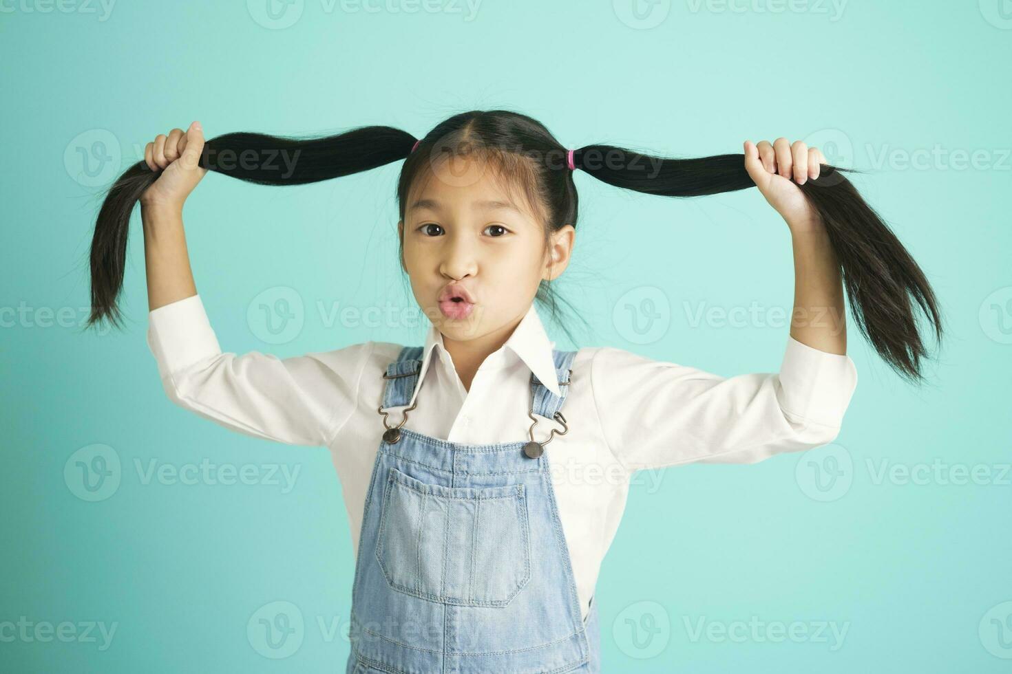 Smiling little girl in glasses pretty long hair, hold hair above her , look at camera. photo