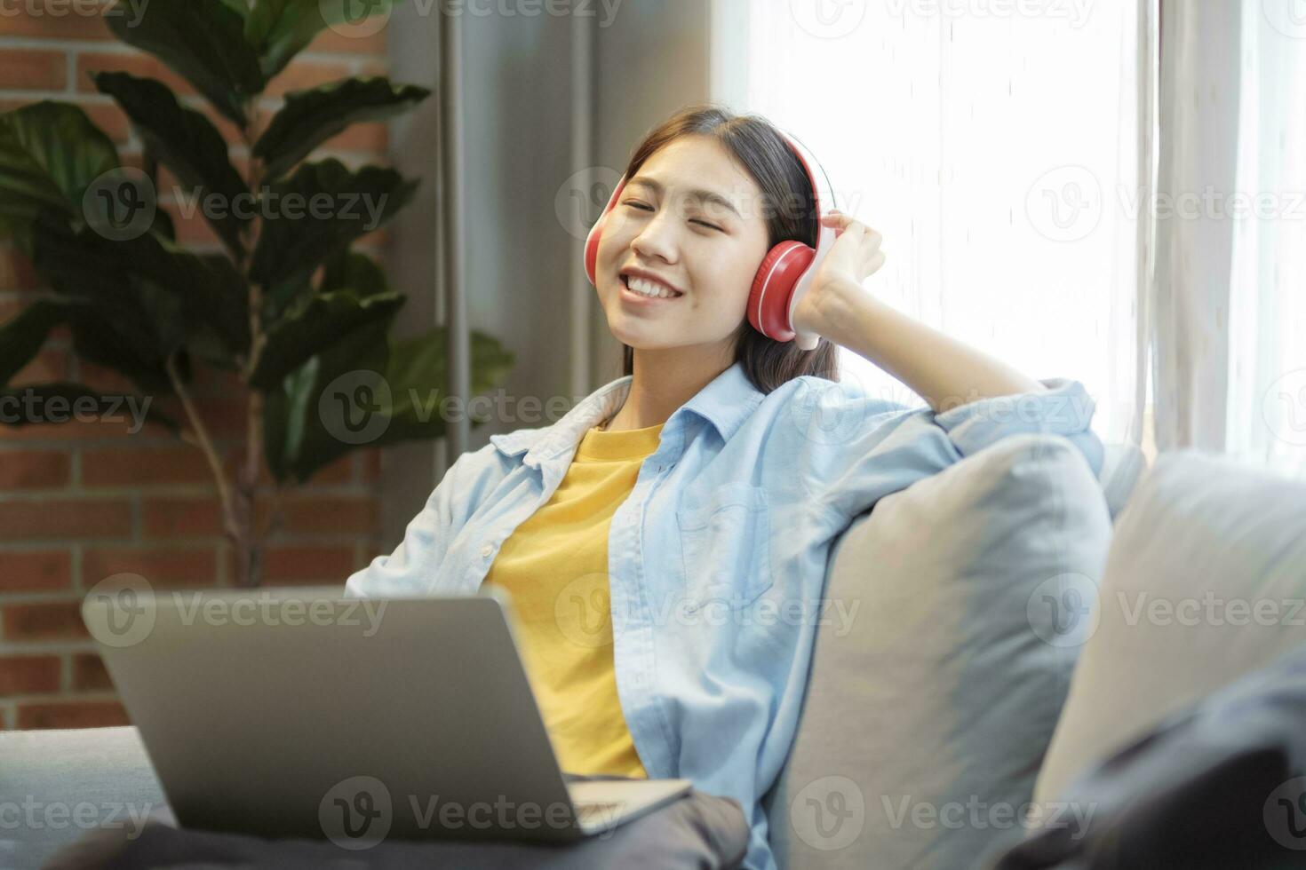 contento asiático mujer escuchando a música mientras inclinado espalda en sofá. foto