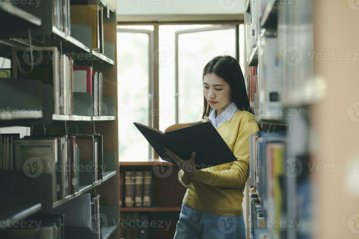 Student standing and reading book at library. photo