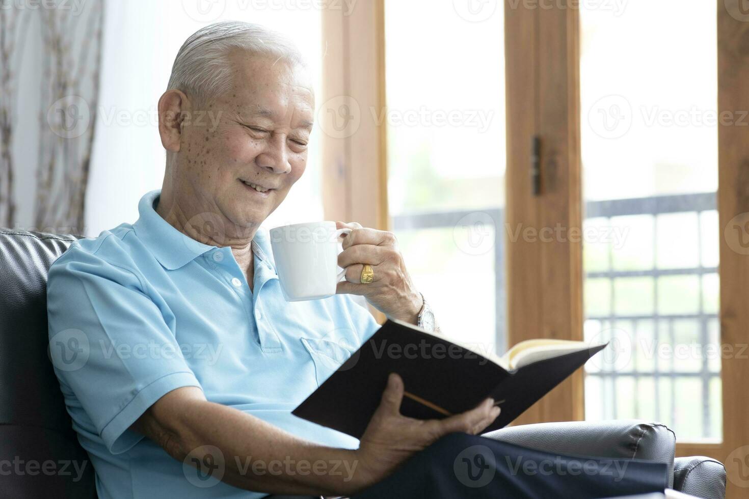 relajarse mayor hombre sentado en sofá y leyendo interesante libro en vivo habitación. foto