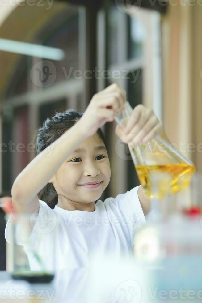 Little girl in lifting and looking at substance in tube in chemistry science class. photo
