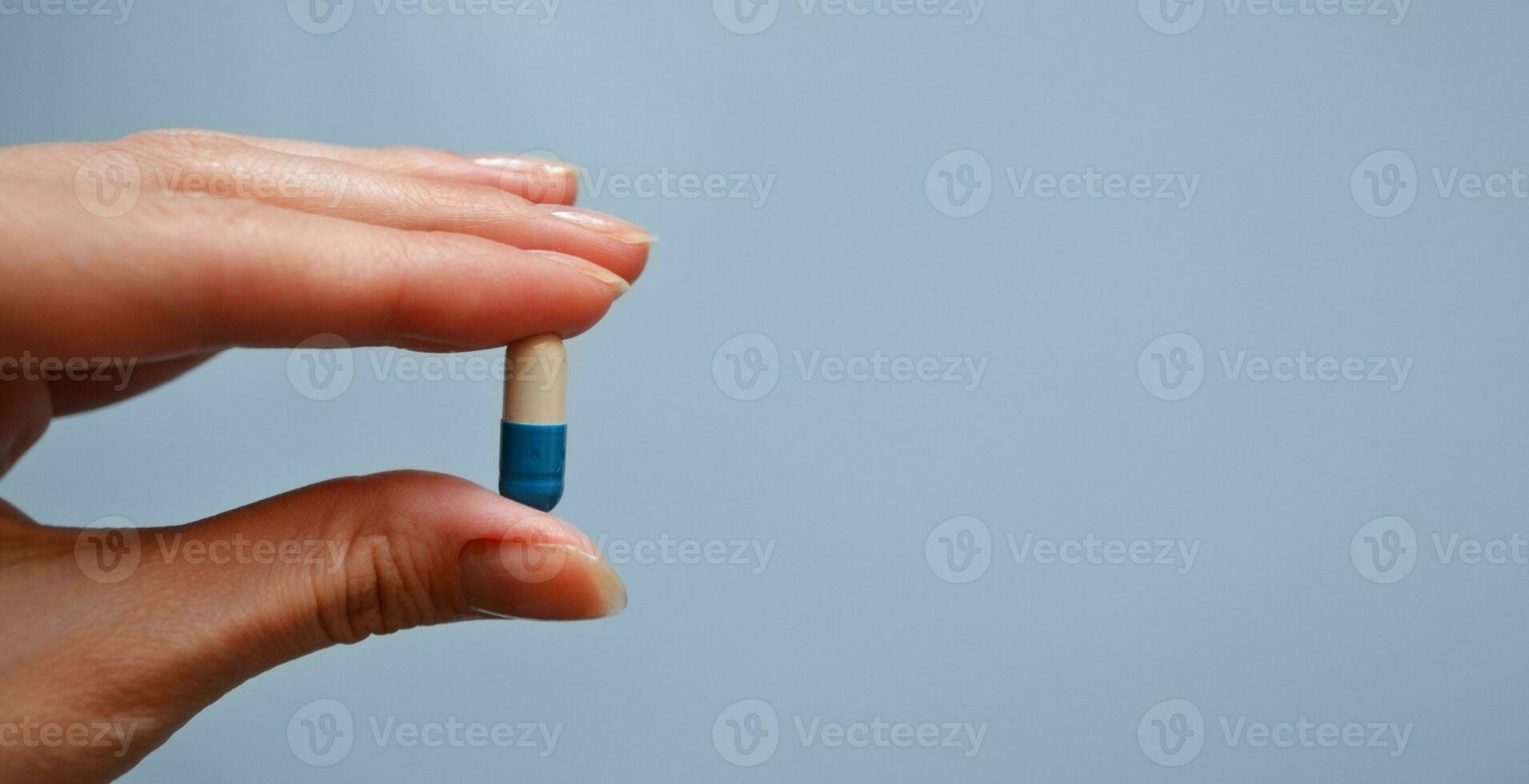 cápsula Entre el dedos en un azul fondo, medicamento, médico del trabajador día, médico cuidado, bandera para el hospital foto