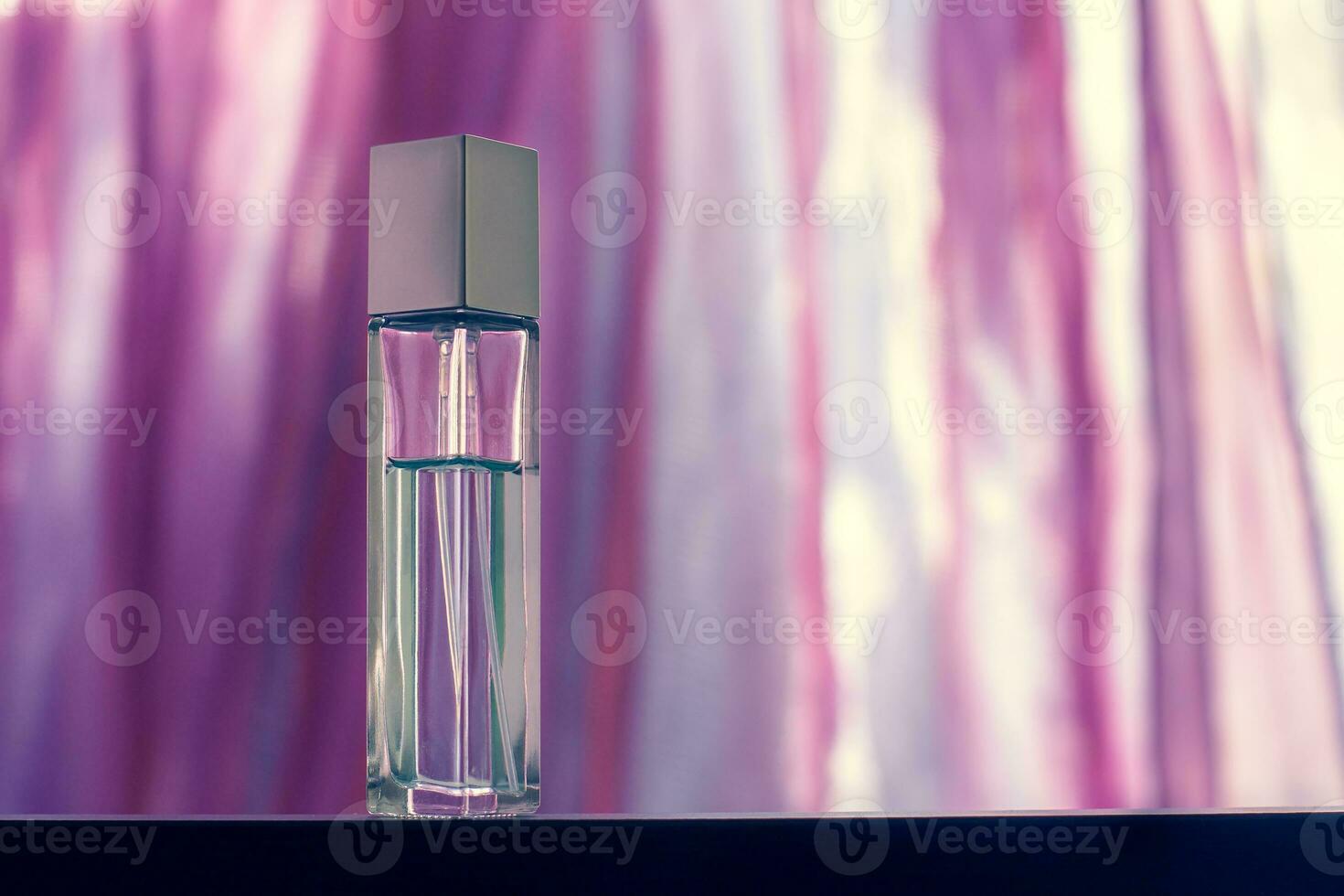 An elongated faceted perfume bottle stands on a blurry light pink background. Glass vial with a metal cap. Blank for mock up. Selective focus. Horizontal. photo