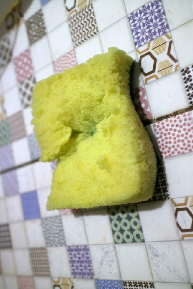 A broken yellow foam used for washing dishes is placed on the tile photo