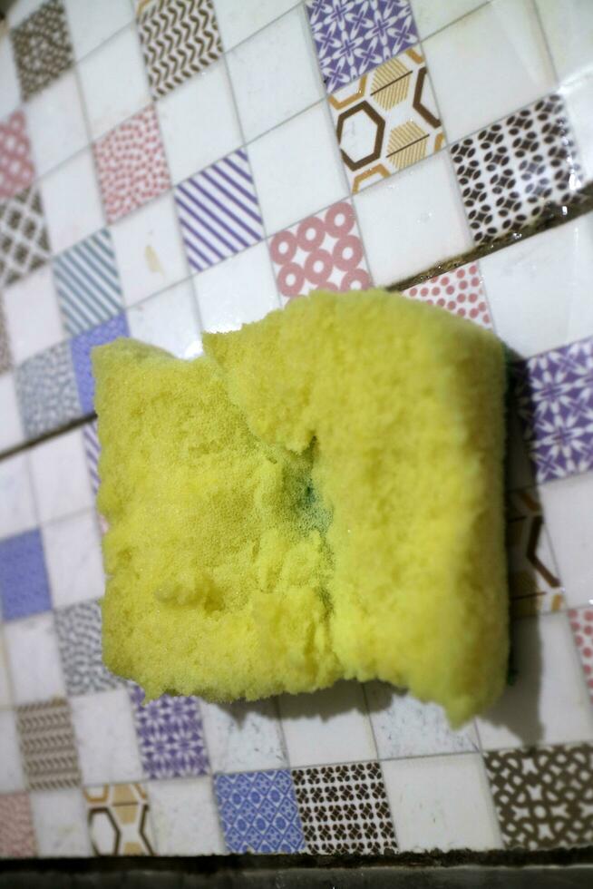 A broken yellow foam used for washing dishes is placed on the tile photo