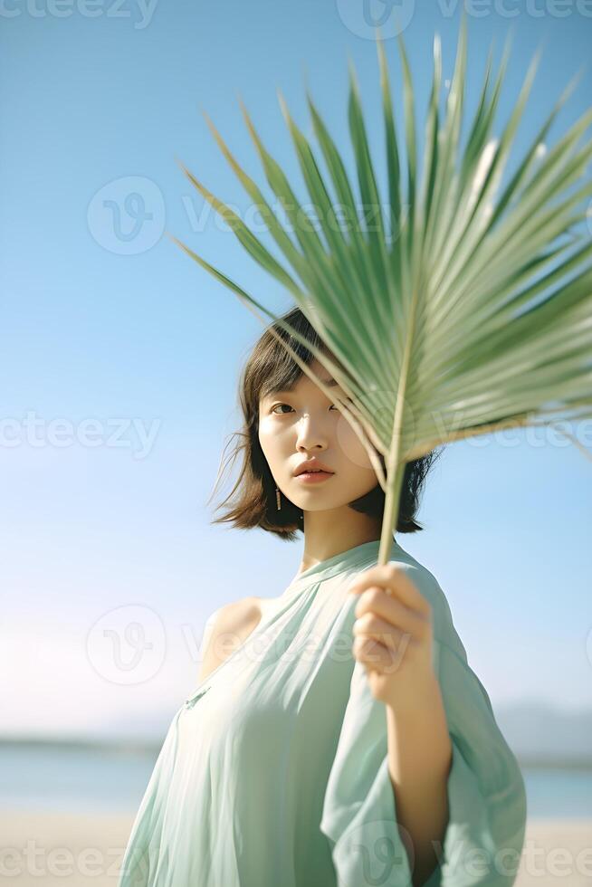retrato de un hermosa asiático mujer participación un palma hoja en el playa. generativo ai foto