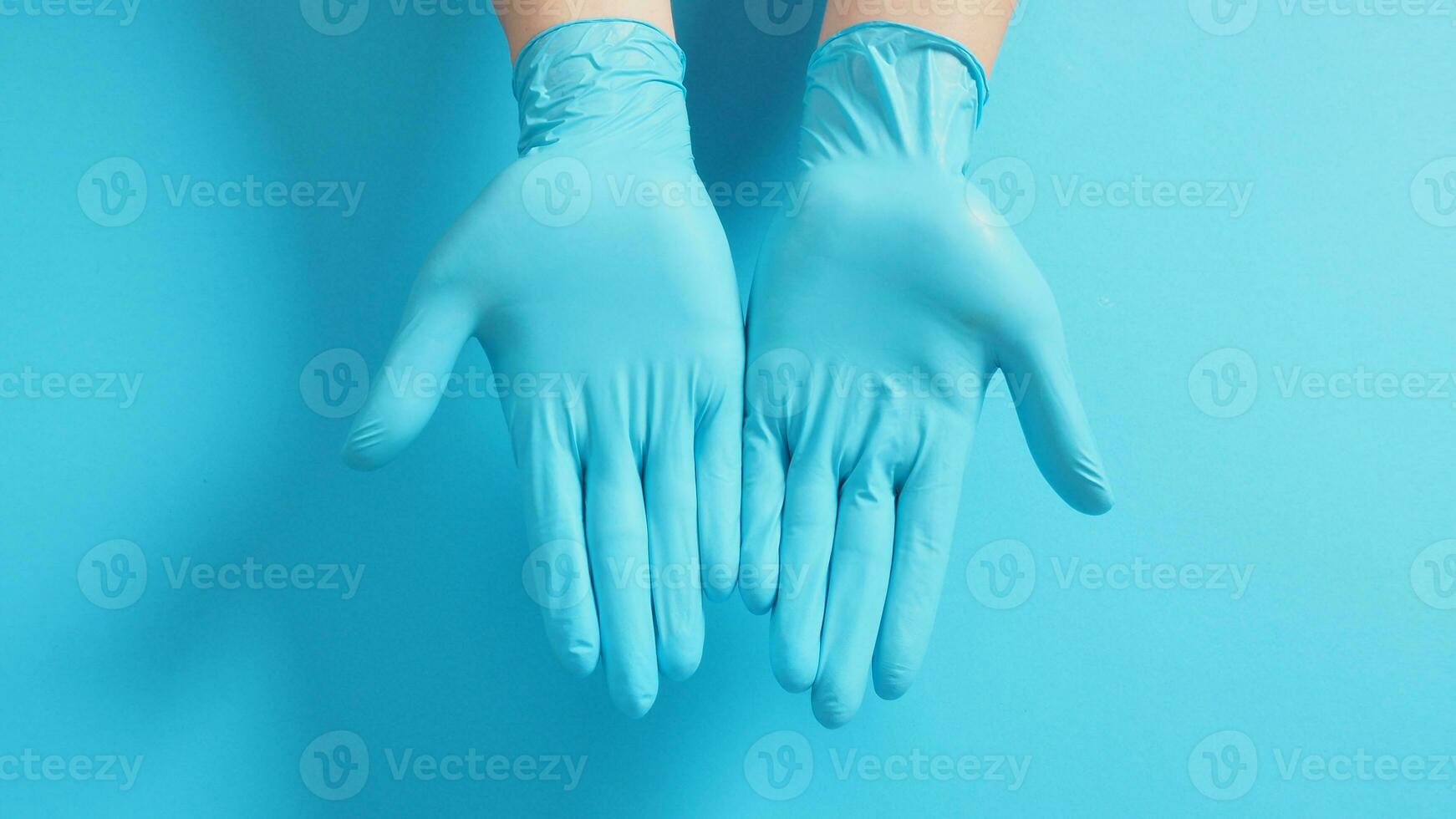 dos mano vestir azul médico guantes en azul antecedentes. foto