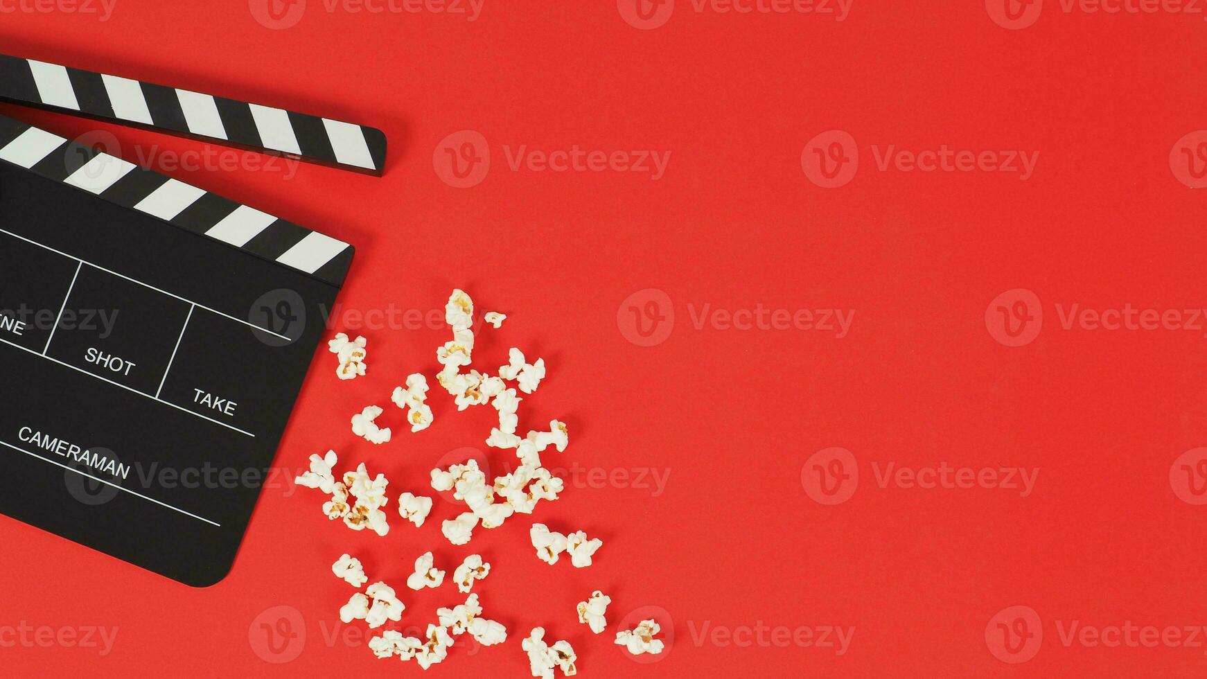 Black Clapper board or movie slate and popcorn on a red background.  New photo