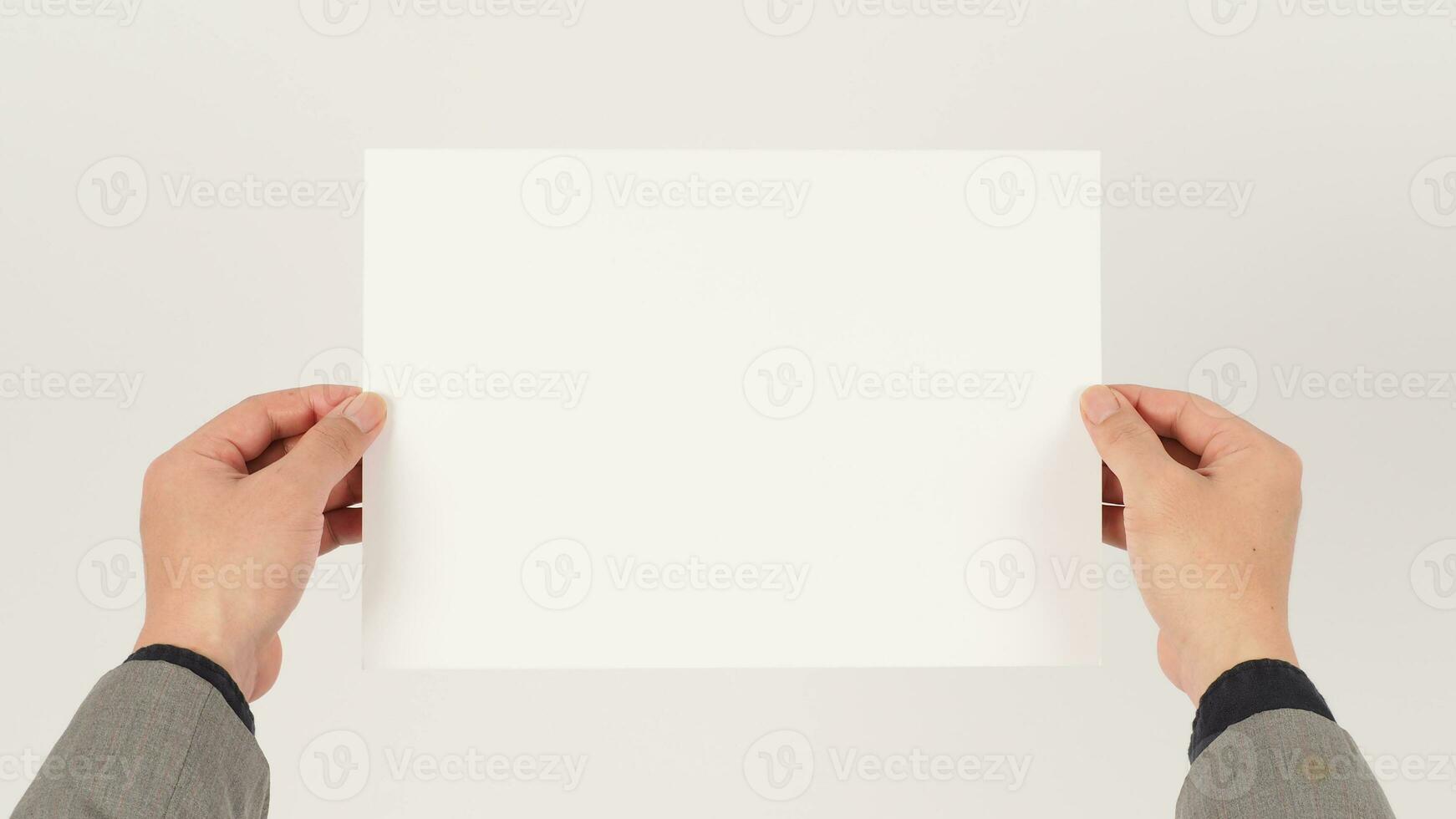 Space for text. The hand is wearing a gray suit and holding blank board A4 paper on white background. photo