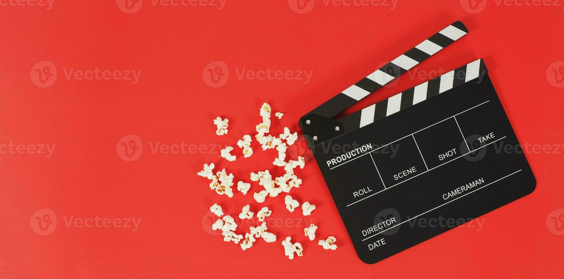 Black Clapper board or movie slate and popcorn on a red background. photo