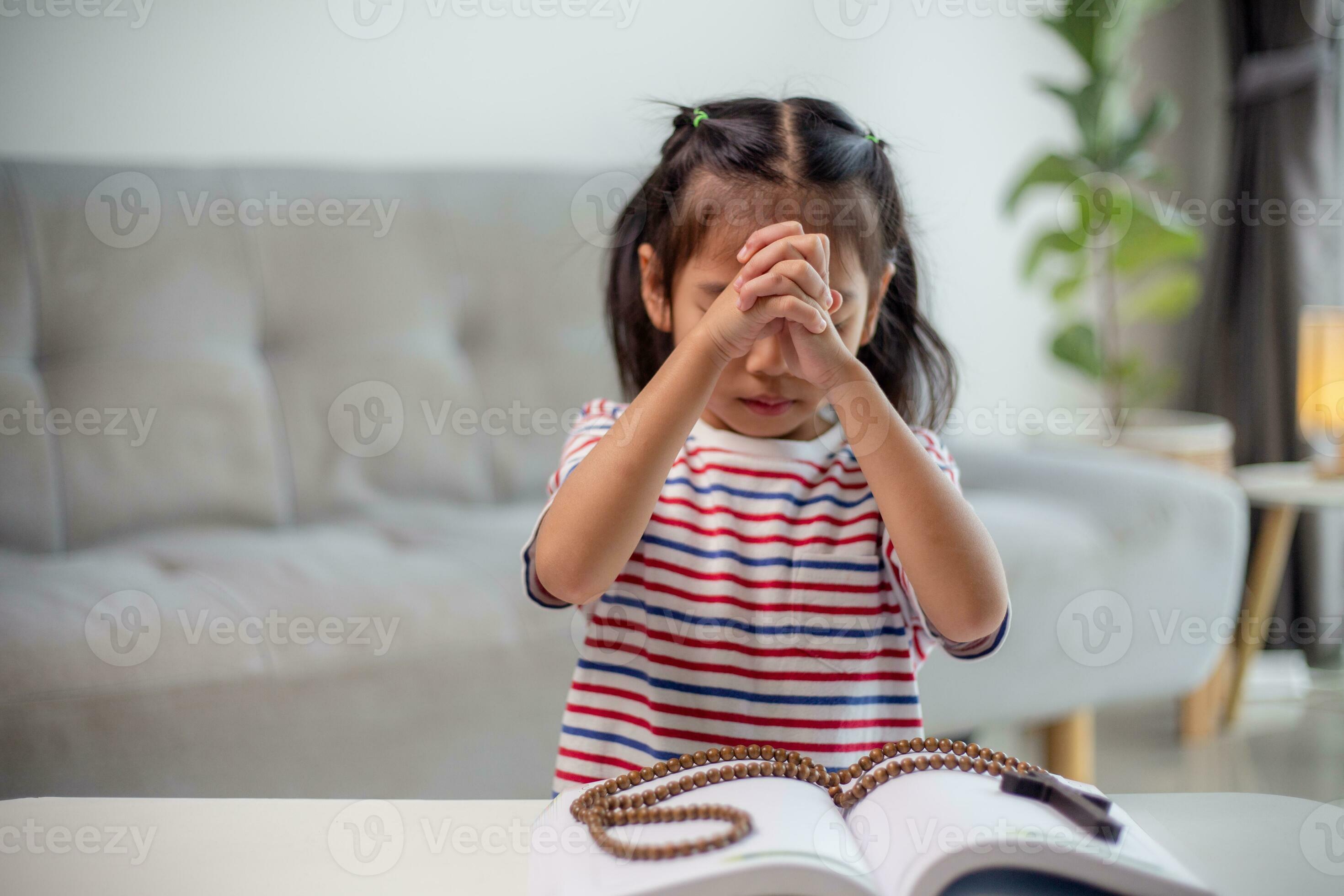 Christian concept. Little Asian girl praying withholding the cross