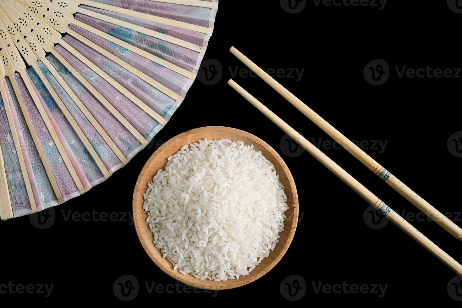 Raw white rice, hand fan and chopsticks on black background. Long uncooked rice in a wooden plate. photo