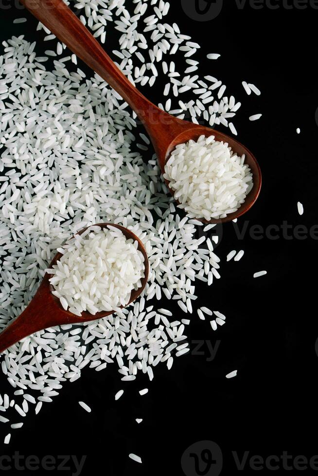 White rice in wooden spoons on black background. Raw grains of long rice. photo