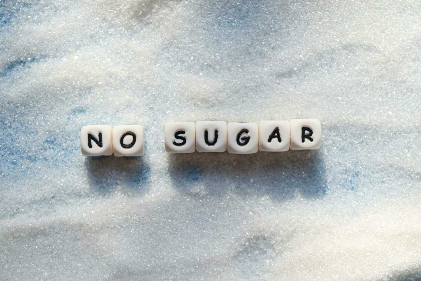 no sugar text blocks with white sugar on wooden background, suggesting dieting and eat less sugar for health concept photo
