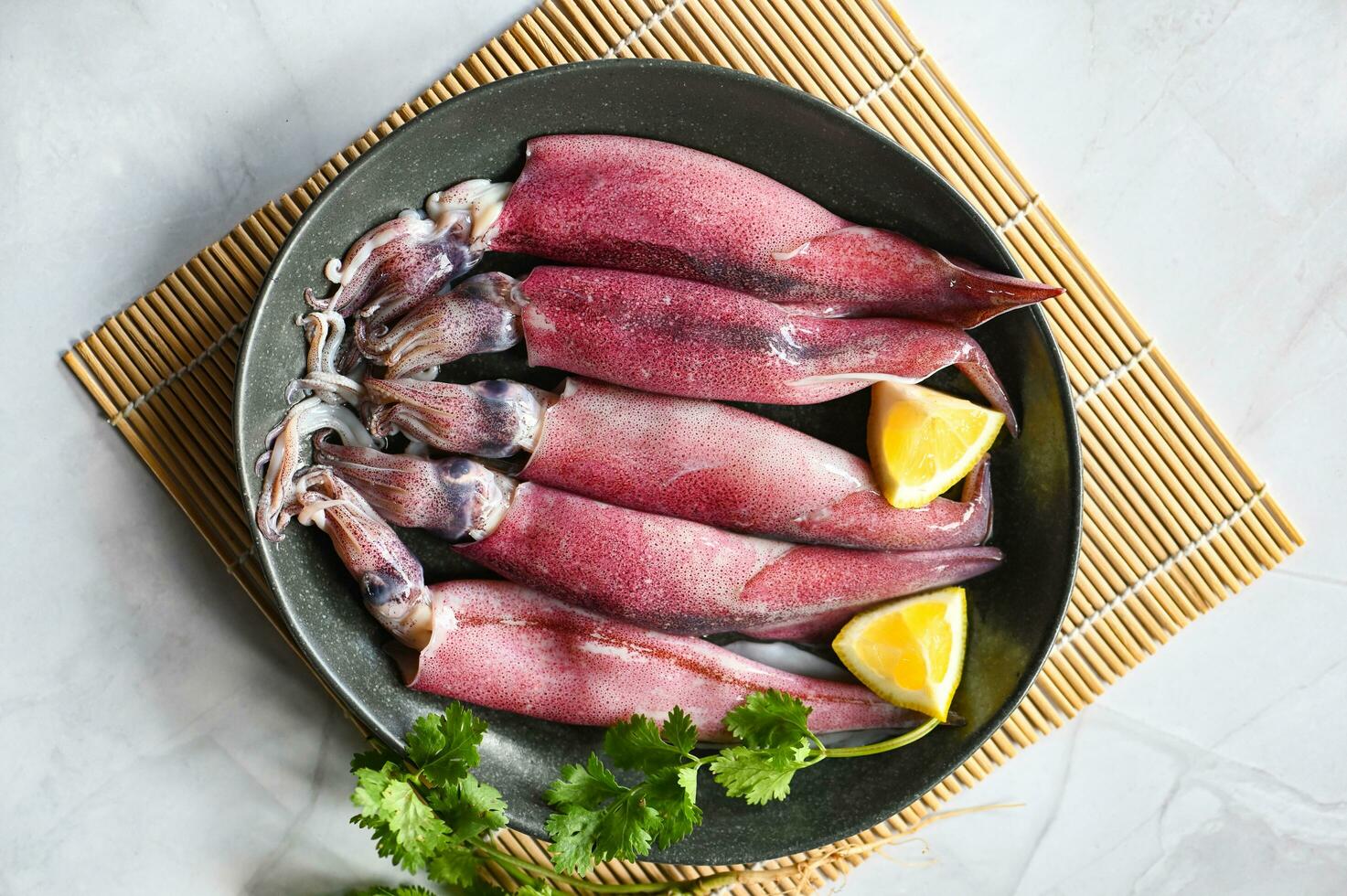 Raw squid on plate with salad spices lemon on wooden background, fresh squids octopus or cuttlefish for cooked food at restaurant or seafood market photo