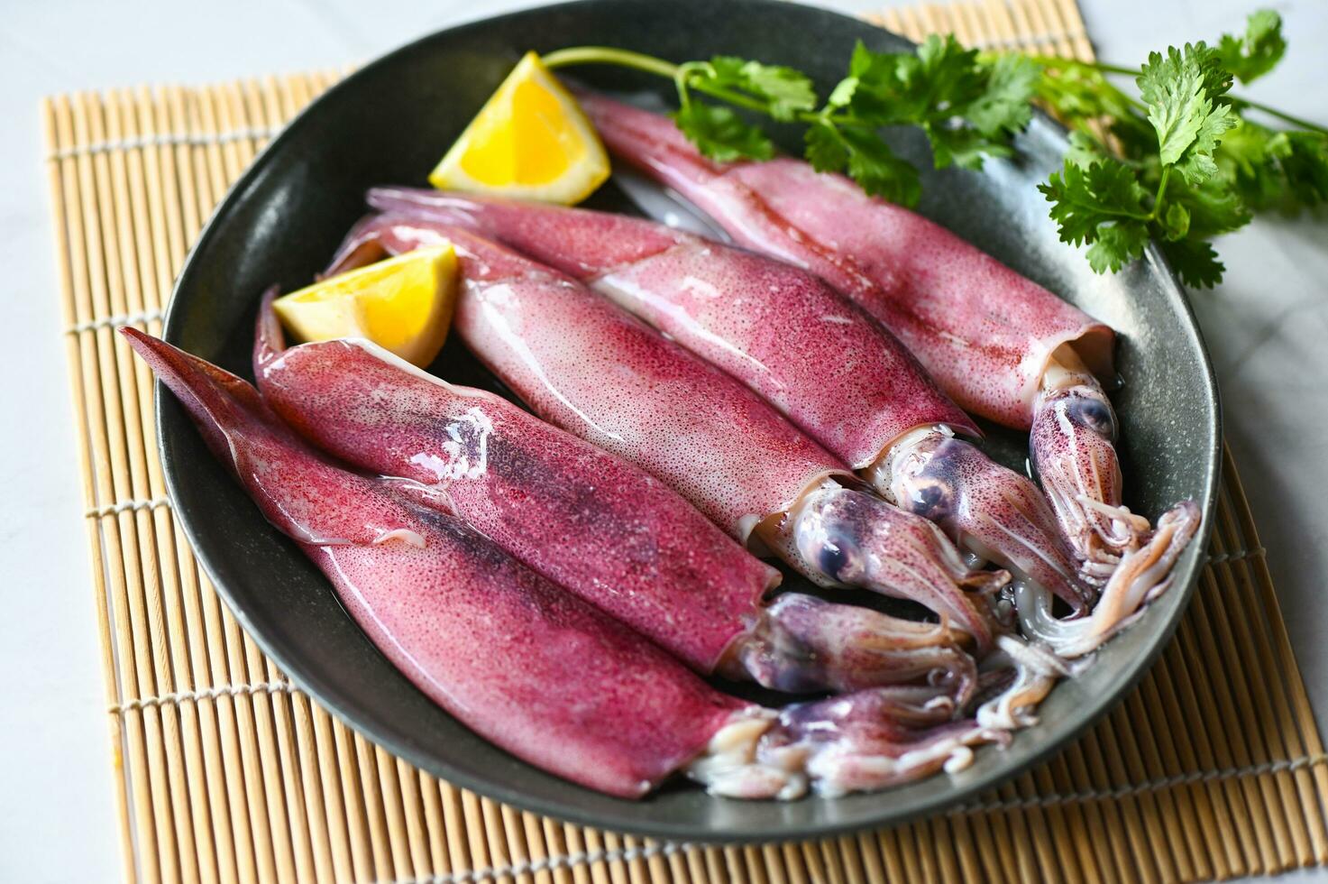 Raw squid on plate with salad spices lemon on the dark plate background, fresh squids octopus or cuttlefish for cooked food at restaurant or seafood market - top view photo