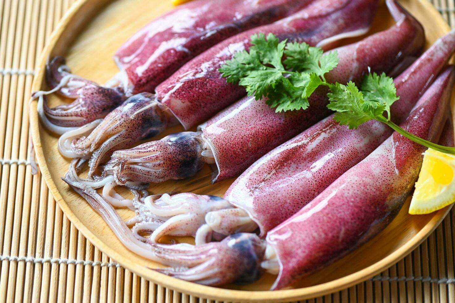 Raw squid on plate with salad spices lemon on wooden background, fresh squids octopus or cuttlefish for cooked food at restaurant or seafood market photo