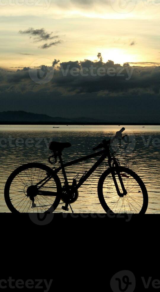 silhouette of a bicycle against the background of the sunset on the lake photo