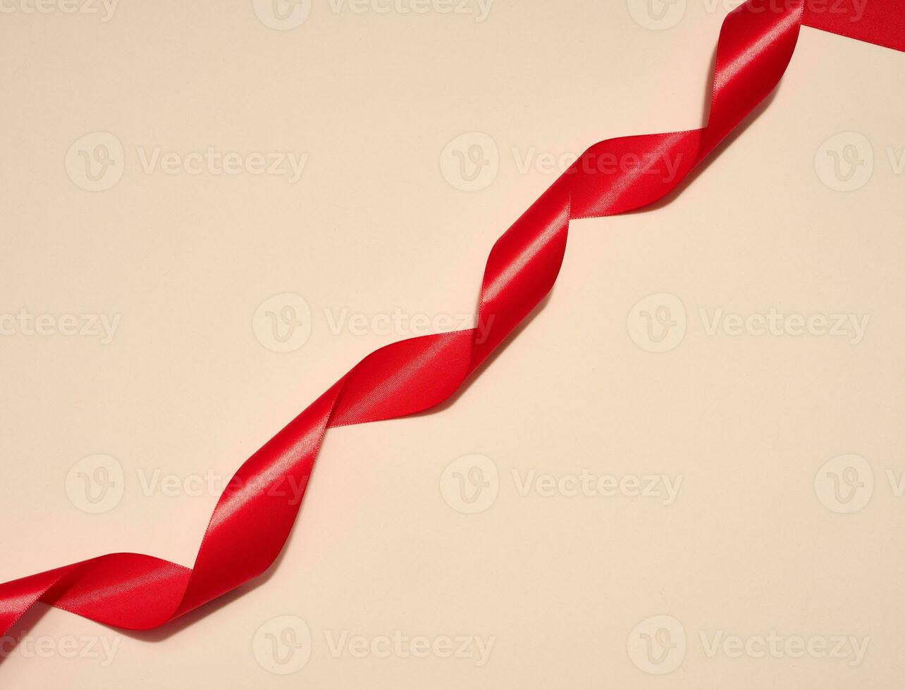 Red silk ribbon on a beige background, top view photo