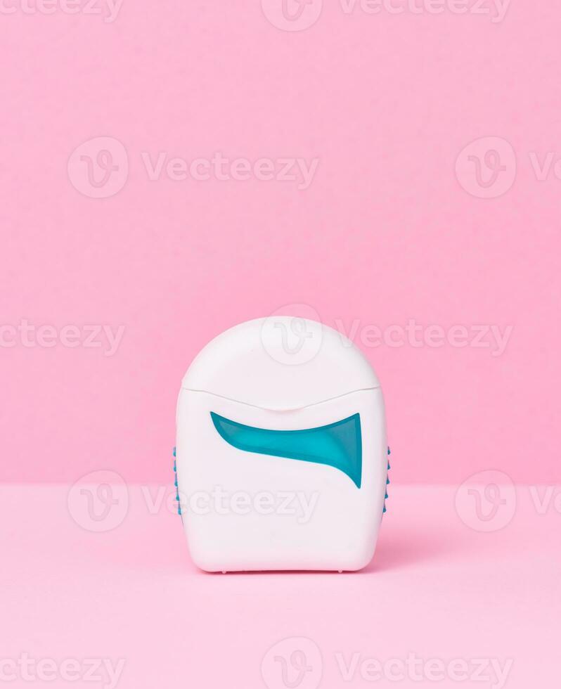 White plastic packaging with dental floss on a pink background, close up photo