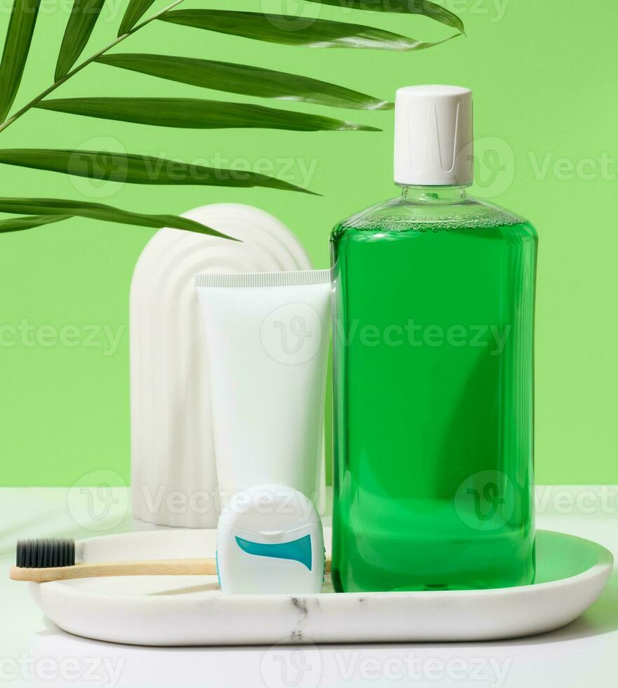 Refreshing mouthwash in a transparent plastic bottle and dental floss, white tube on a green background photo