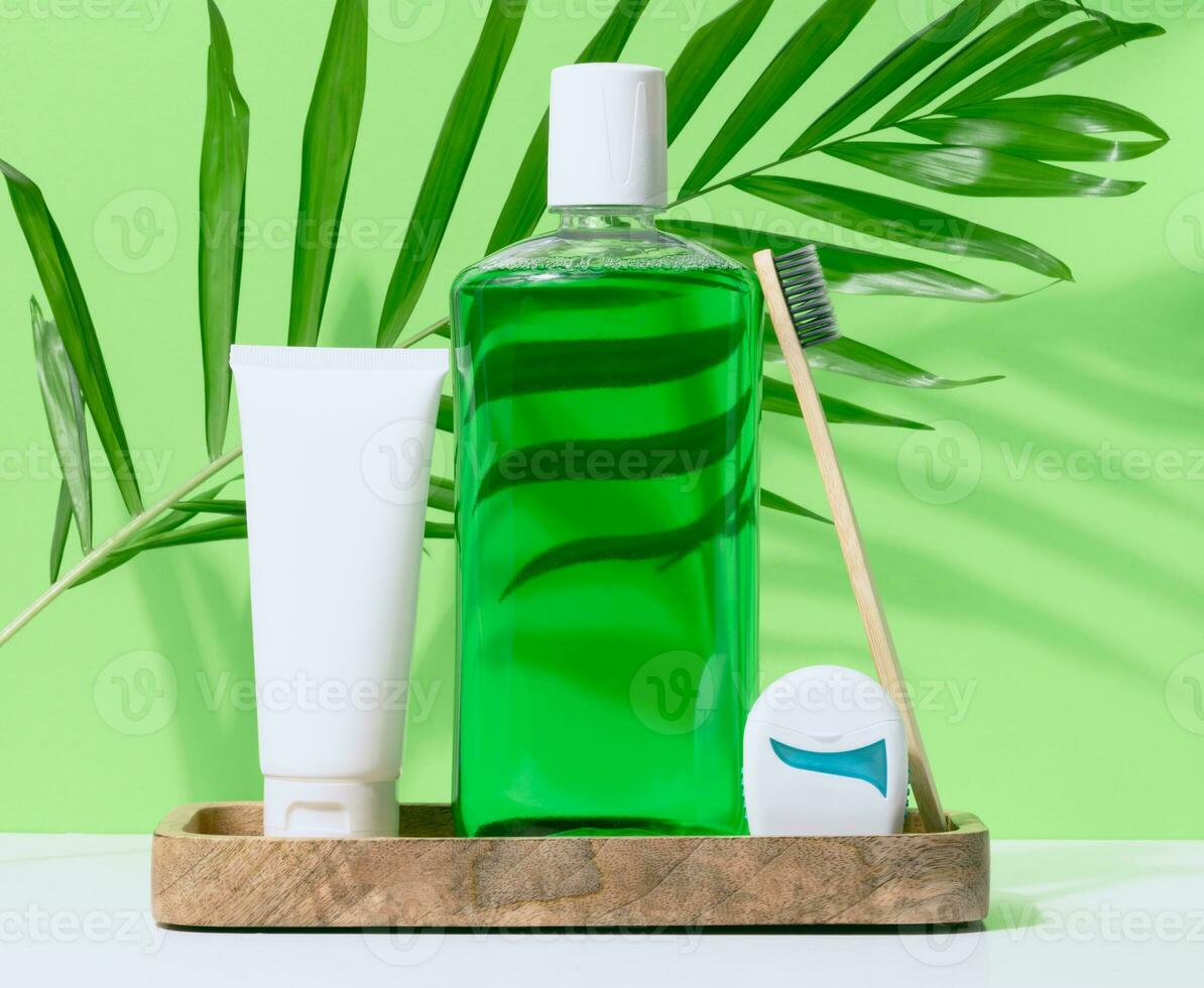 Refreshing mouthwash in a transparent plastic bottle and dental floss, white tube on a green background photo