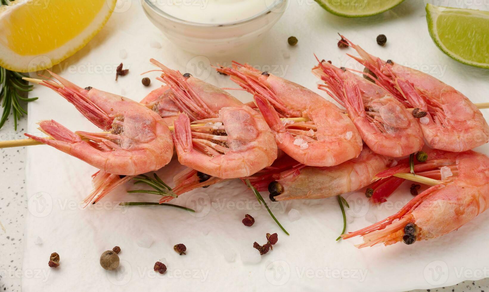 Shrimps strung on wooden sticks, soy sauce and spices on a white table, top view photo