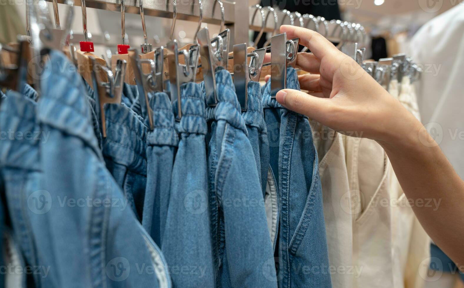 Woman shopping denim pants in clothing store. Woman choosing clothes. Jeans on hanger hanging on rack in clothing store. Fashion retail shop inside shopping mall. Clothes on hangers in a clothes shop. photo