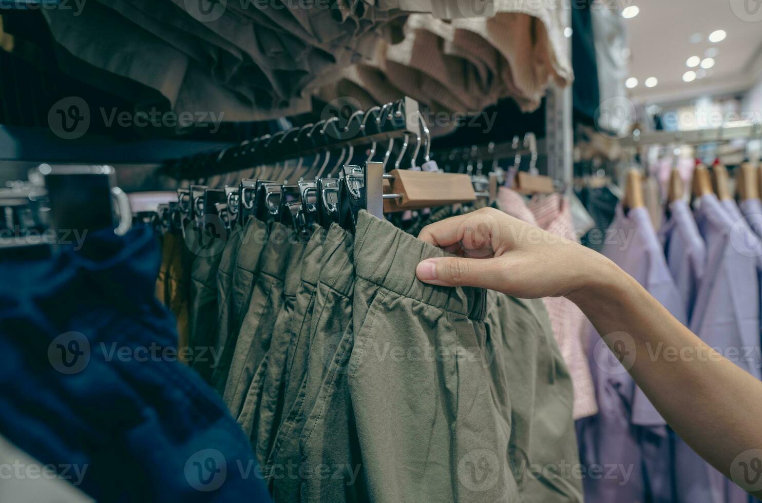 Woman shopping green shorts in clothing store. Woman choosing clothes. Shorts on hanger hanging on rack in clothing store. Fashion retail shop inside shopping mall. Clothes on hangers in clothes shop. photo