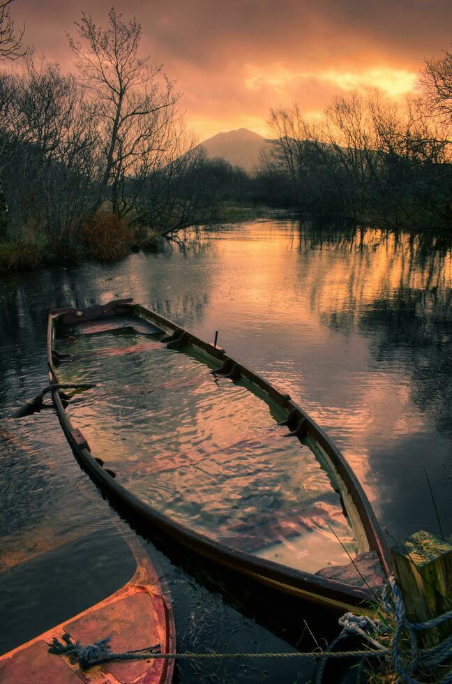 Beautiful nature sunset scenery with old wooden sunken boat in the river with mountains in the background at Connemara National park in County Galway, Ireland photo