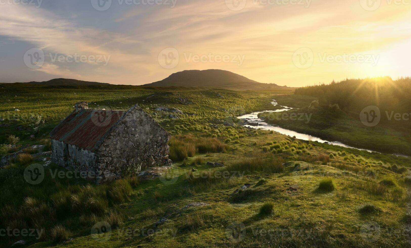 Beautiful sunset scenery of old rusty tin roof cottage on green hill by the river at Connemara National park, county Galway, Ireland photo