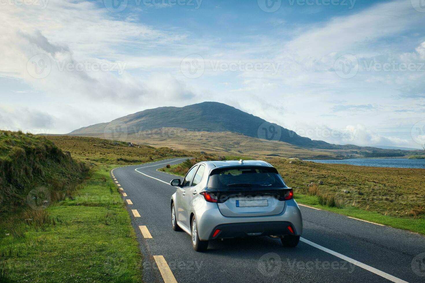 Beautiful landscape scenery with car driving on empty scenic road trough nature by the lough inagh with mountains in the background at Connemara National park in County Galway, Ireland photo