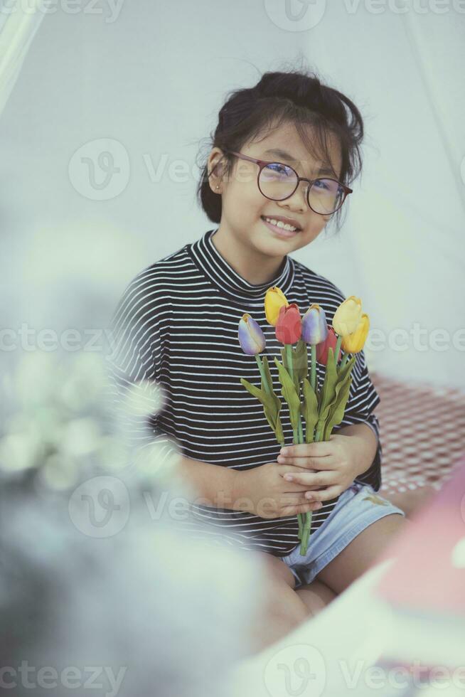 asian kid holding artificial of tulip flower in hand toothy smiling with happiness photo