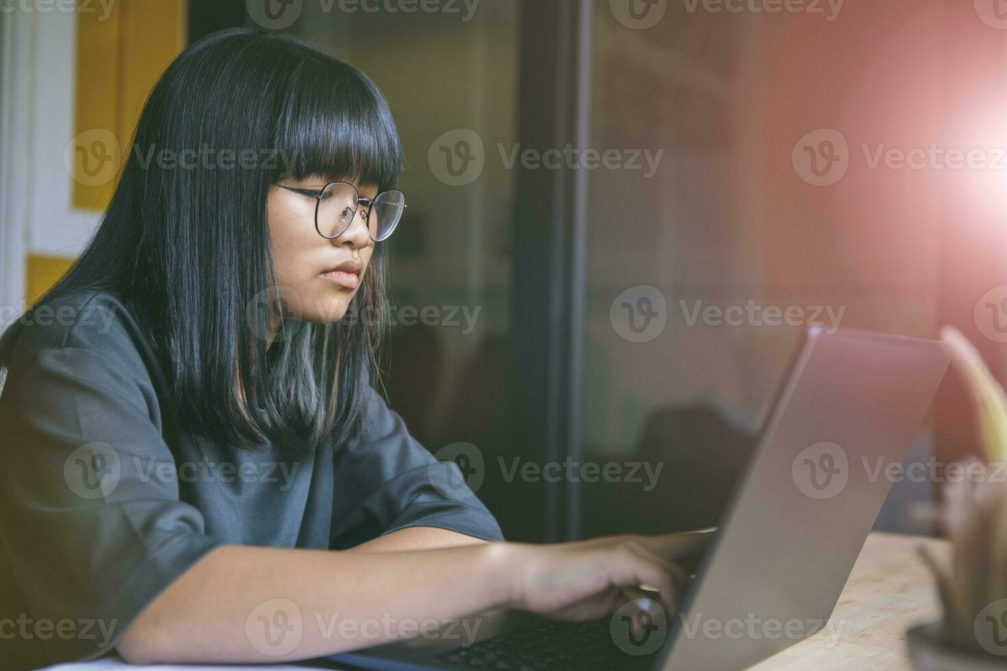 asian teenager sitting in working room and  reading message on computer laptop screen photo
