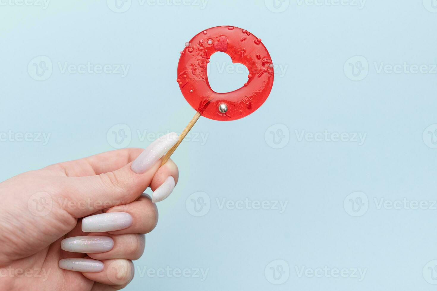 Woman female hand holding heart shaped lollipop on blue background. photo